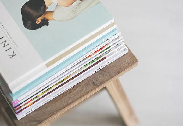 Man sieht einen Stapel Magazine und Zeitschriften ordentlich übereinander gestapelt auf einem Hocker oder Stuhl liegen.