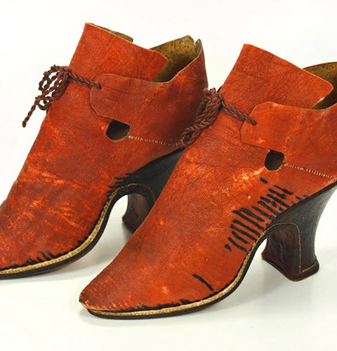 Damenstöckelschuh aus rotem Schafleder mit Resten von Verzierungen aus schwarzen Borten am gesamten Schaft. Die Stepplöcher sind noch sichtbar. Das Vorderteil endet nach oben in großer eckiger Ristlasche. Als Verschluss sind zwei kurze Fersenteillaschen, die mittels eines Bandes über der Ristlasche zusammengebunden wurden. Über dem Sohlenrand ist eine weiße Lederpaspel eingearbeitet. Absatz leicht geschweift, mit schwarzem Leder überzogen und Halbmond-Trittflächen. Sohlen- und Absatzlinie werden durch eine weiße Naht markiert.