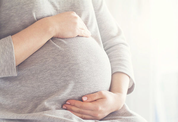 Das Bild zeigt im Zentrum den Bauch einer schwangeren Frau. Sie umfasst den schon ziemlich dicken Bauch mit beiden Händen: eine stützt, die andere liegt oben auf der Kugel. Vielleicht versucht sie die Bewegungen des Kindes zu fühlen.