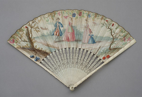 Faltfächer mit 100° Öffnungswinkel von 21 durchbrochenen Elfenbeinstäben, der zusammengelegt wie ein Bündel Stäbe erscheind. Das Blatt aus Papier ist vollständig in Aquarellfarben mit kleine Gesellschaft (Kavalier, Schalmei spielend mit zwei Damen und einem Kind vor einer Küstenlandschaft) bemalt. Flankiert wird die Szene von zwei Bäumen, Blütenranken, Kirschen, Käfer, Pflaumen. Ein Rahmen aus Blumenranken umgibt die Szene. Auf der Rückseite sieht man ein Ruderboot und Segelboote, Dorn: Messing mit Perlmutt belegt. (KSDW)