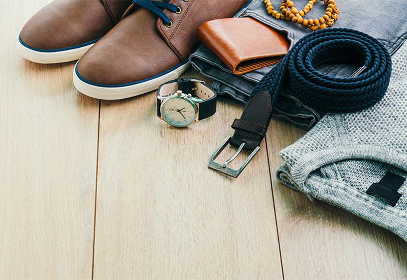 Auf dem Fußboden liegen Kleidung und Accessoires eines jungen Mannes. Ordentlich zusamengelegt sieht man einen Pullover, eine Jeans plus Gürtel, ein paar Schuhe, sowie ein Portemonnaie, eine Uhr und eine Kette oder ein Armband, vermutlich aus Holzperlen.